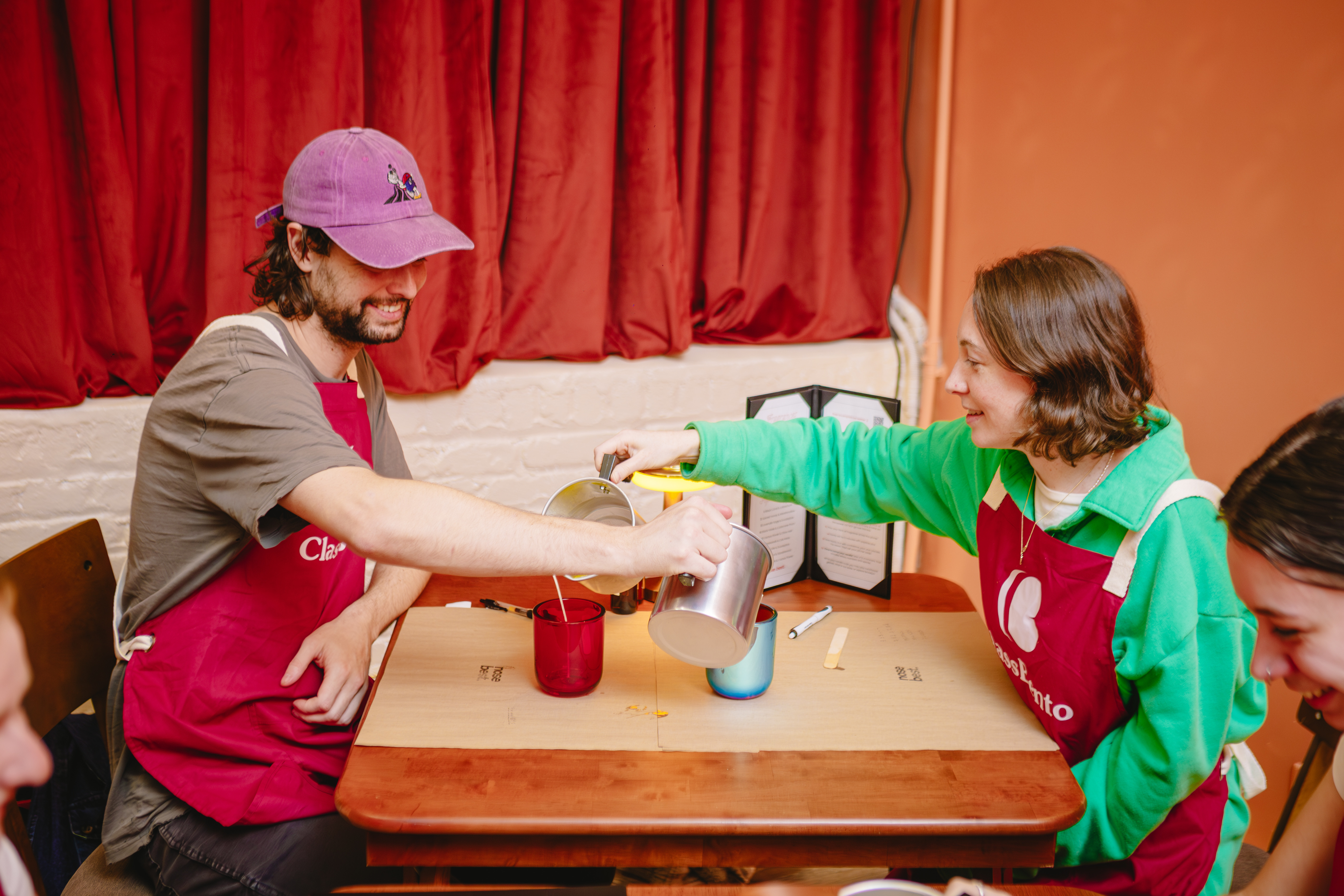 Couple in aprons pouring melted wax into candle jars